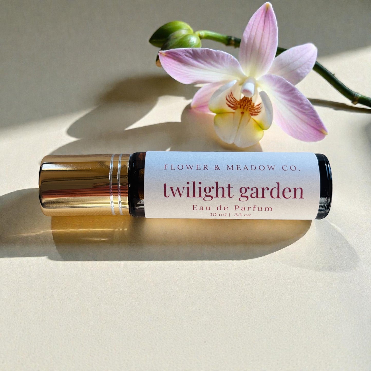 Roll-on bottle of 'Twilight Garden' eau de parfum from Flower & Meadow Co. with a pink orchid on a light background.