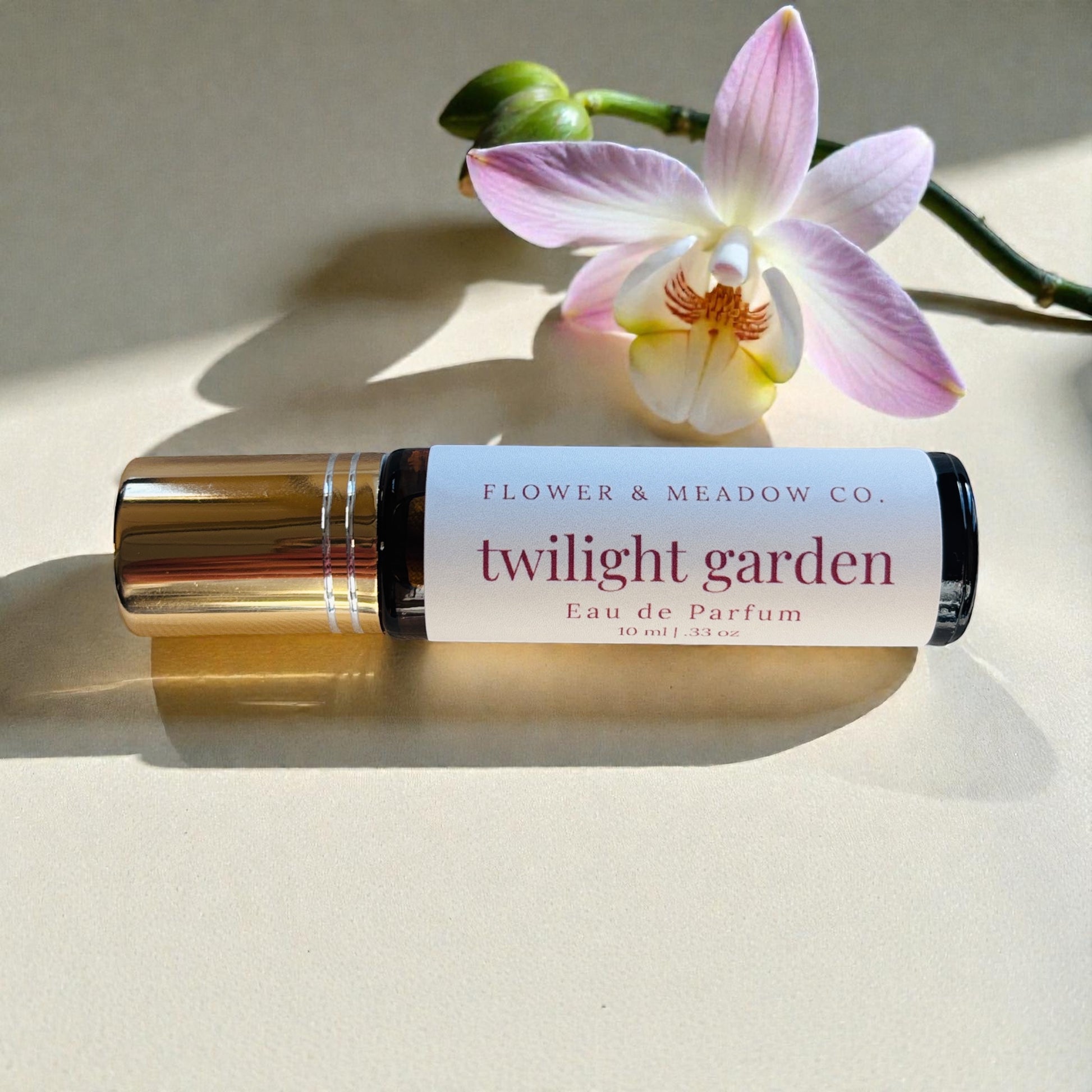 Roll-on bottle of 'Twilight Garden' eau de parfum from Flower & Meadow Co. with a pink orchid on a light background.
