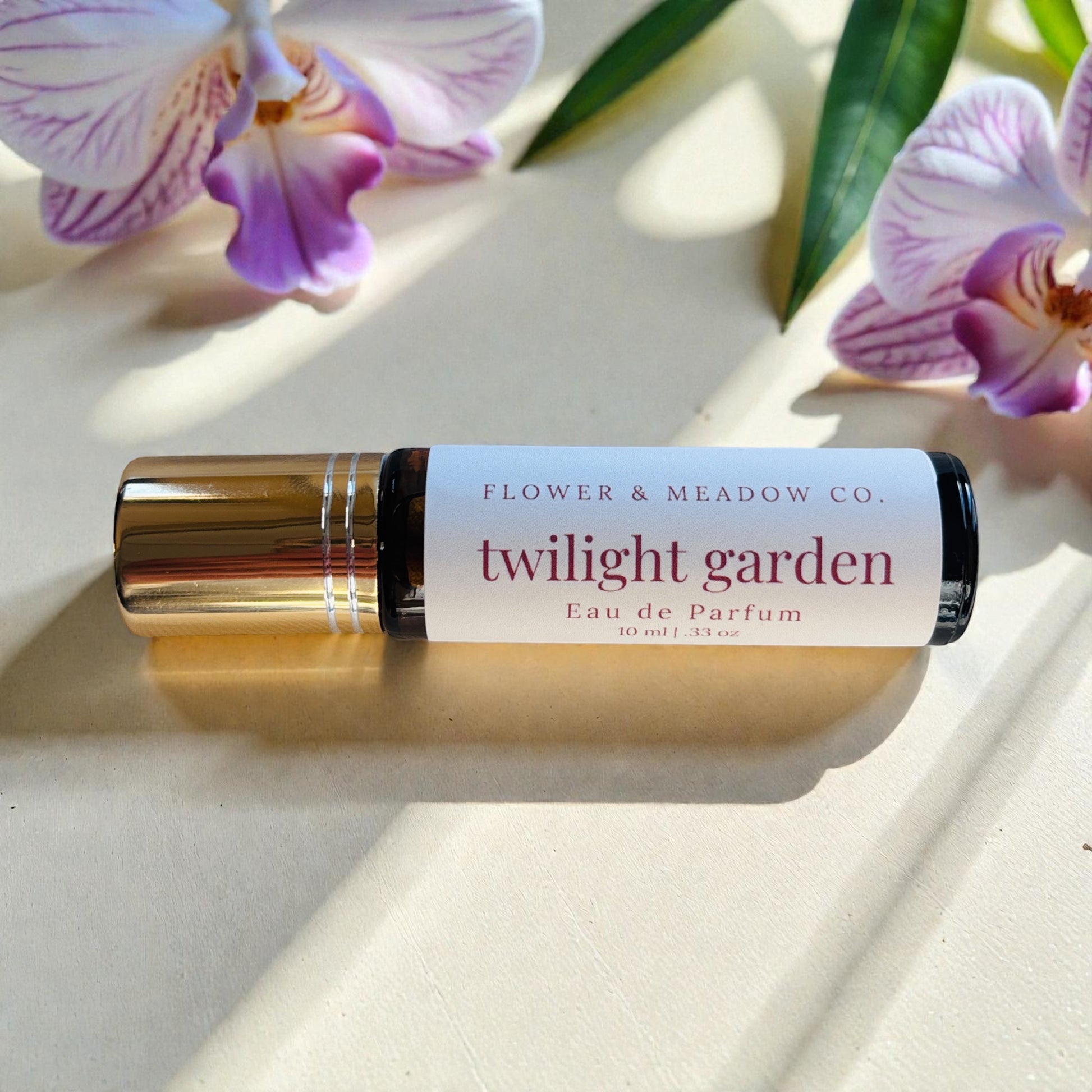 Roll-on perfume bottle labeled 'twilight garden' by Flower & Meadow Co. with purple flowers in the background.